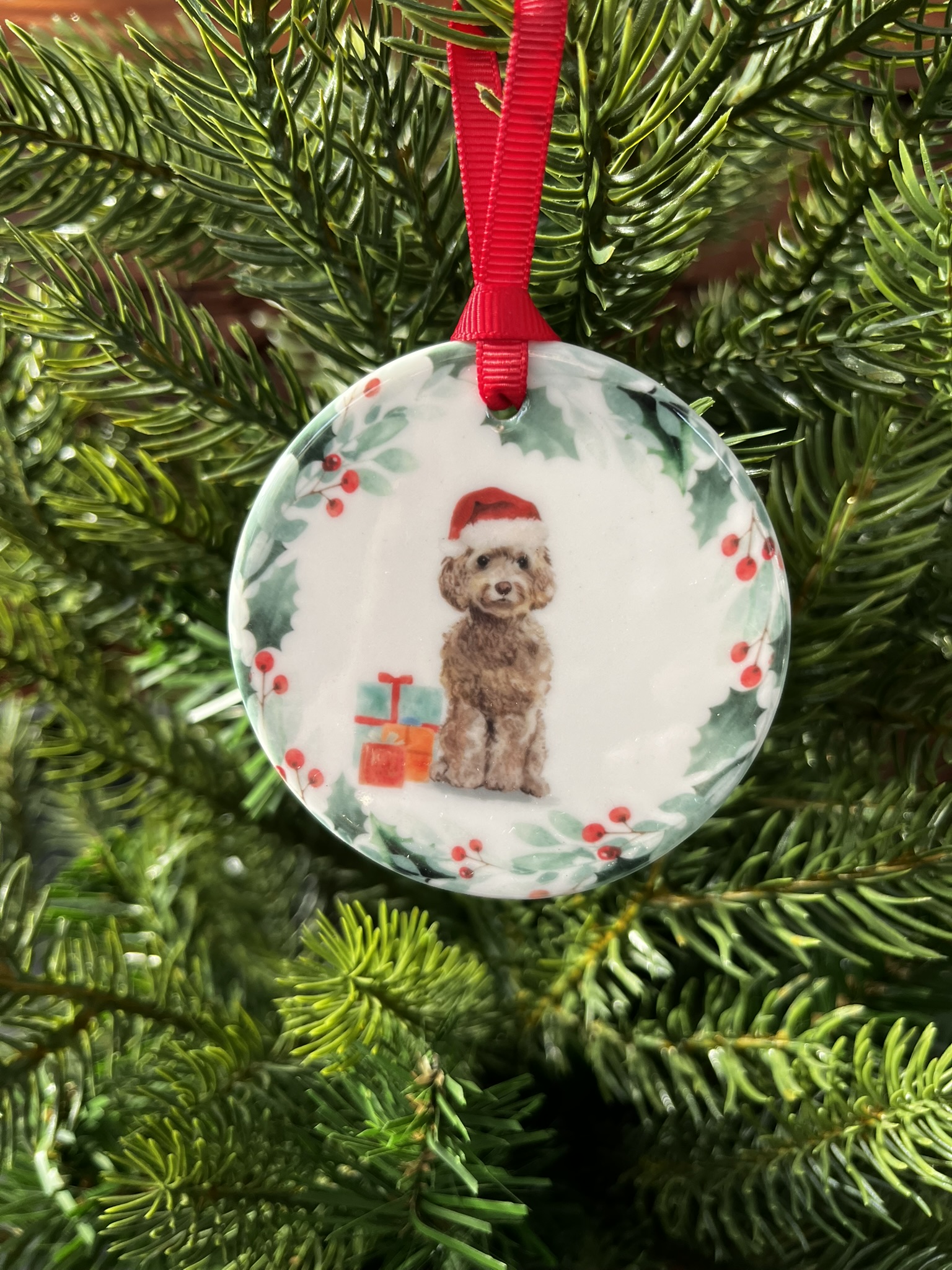 Ceramic hanging decoration with an image of a brown cockapoo wearing a Christmas hat.